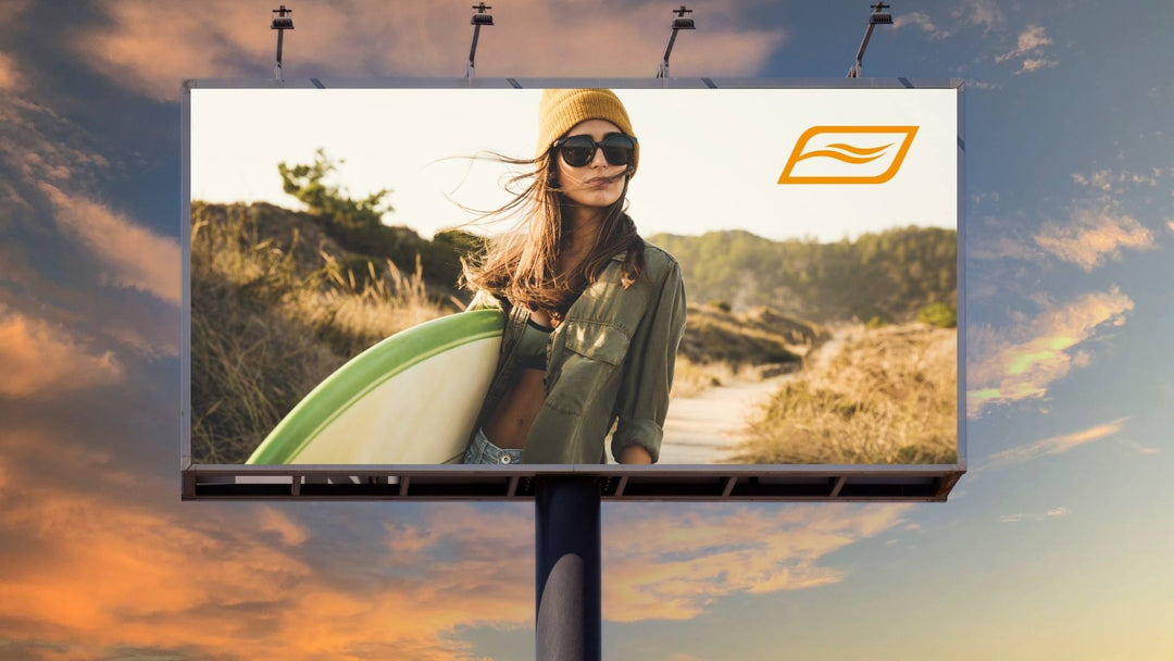 Werbetafel bei Sonnenuntergang mit dem Bild einer jungen Frau mit Sonnenbrille und Mütze, die ein Surfbrett trägt und an einem sandigen Küstenweg steht. Oben rechts ist ein stilisiertes Logo mit einer Wellenform zu sehen.